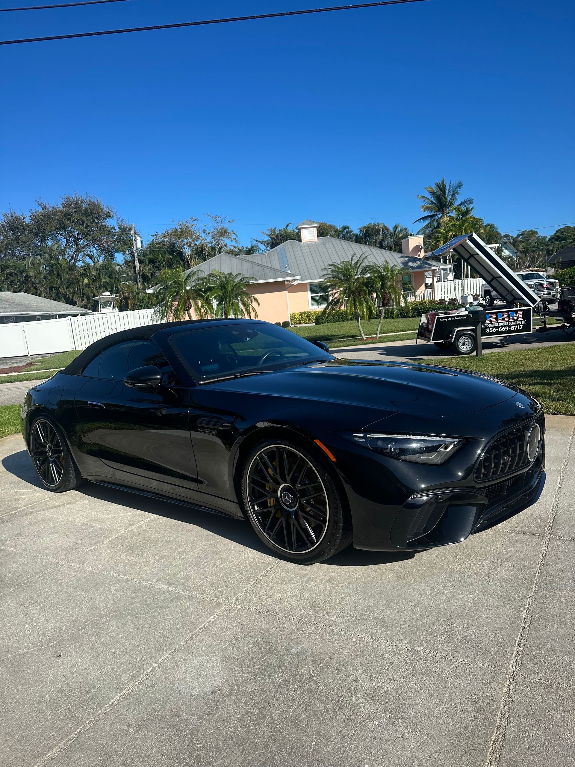 A black sports car is parked on the side of the road in front of a house.