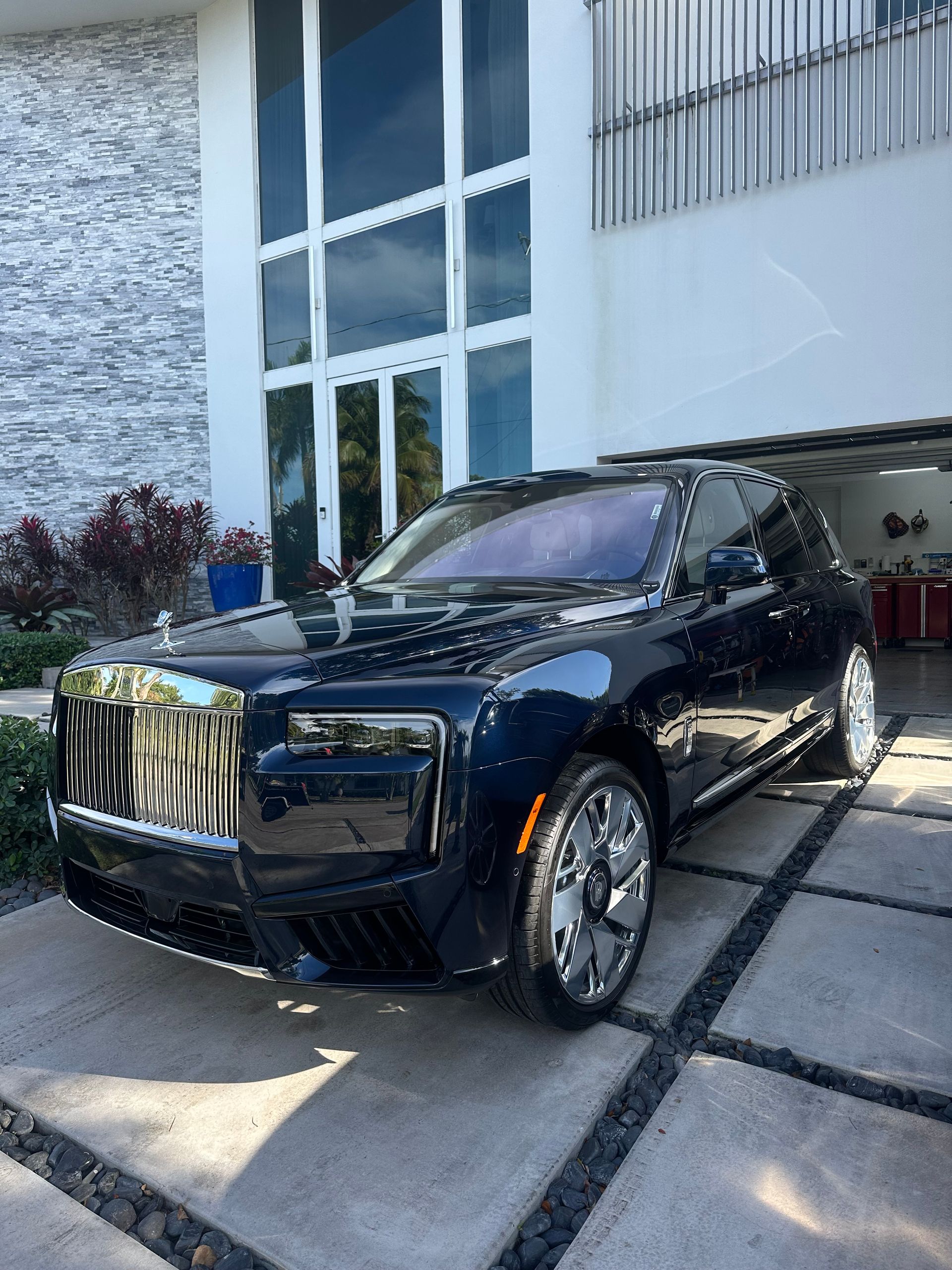 A black sports car is parked in front of a house next to a palm tree.