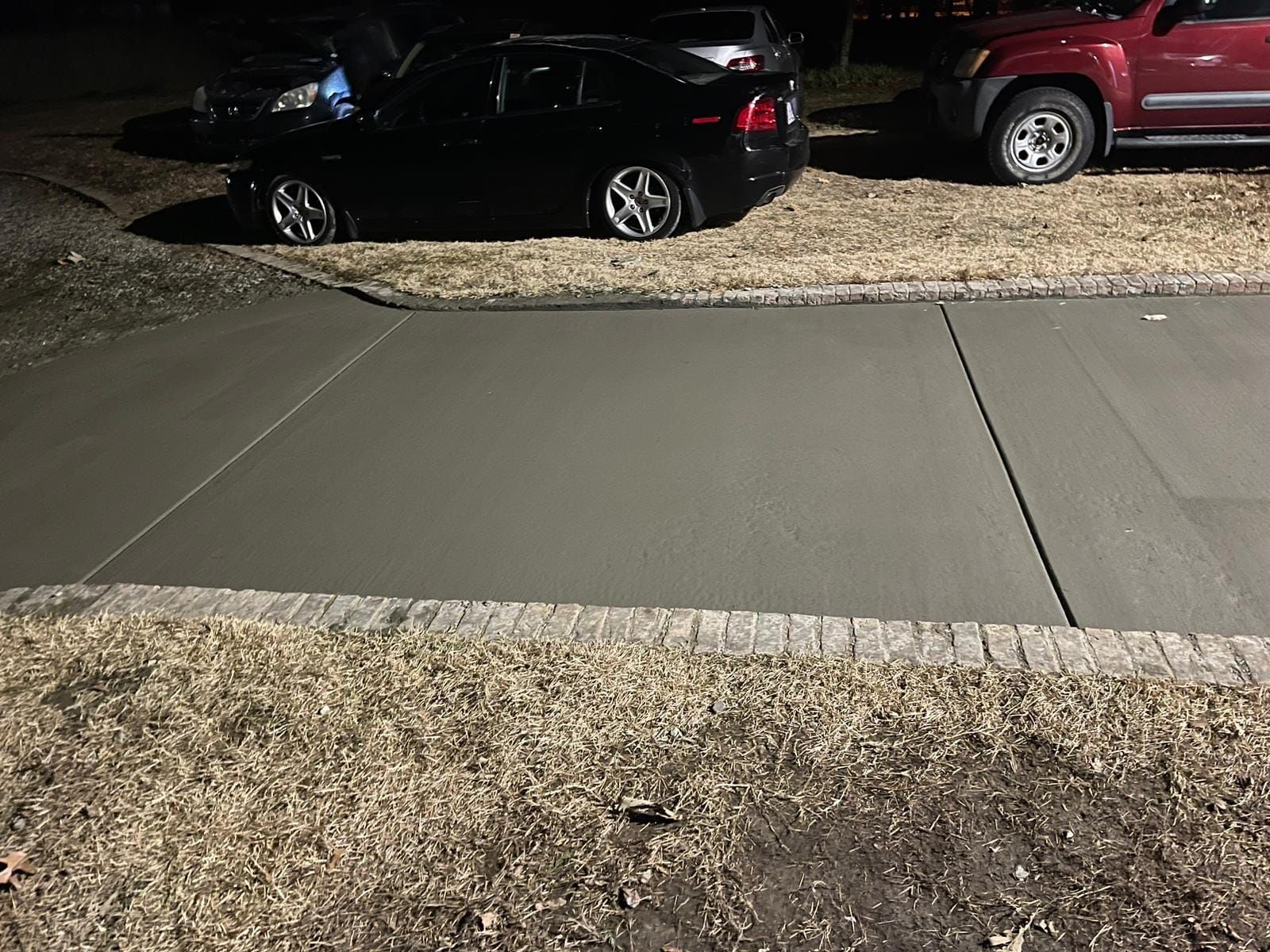 A black car is parked in a driveway next to a red truck.