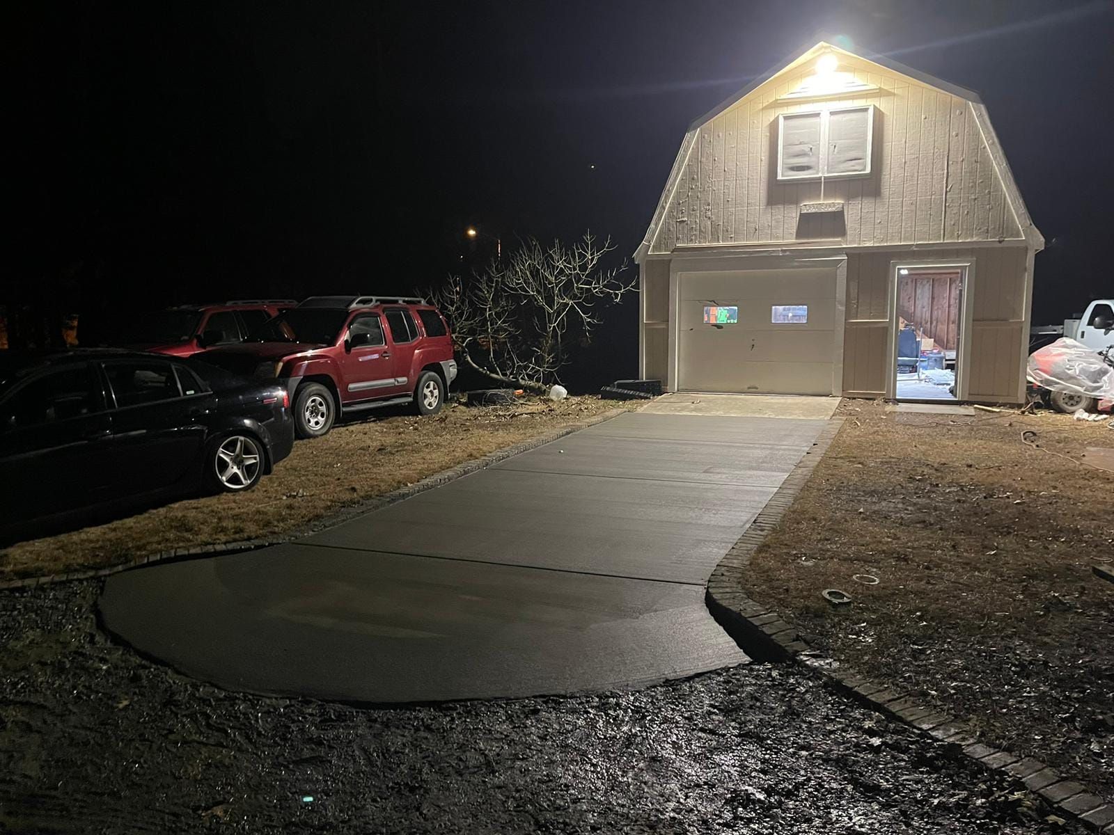 A barn is lit up at night with cars parked in front of it.