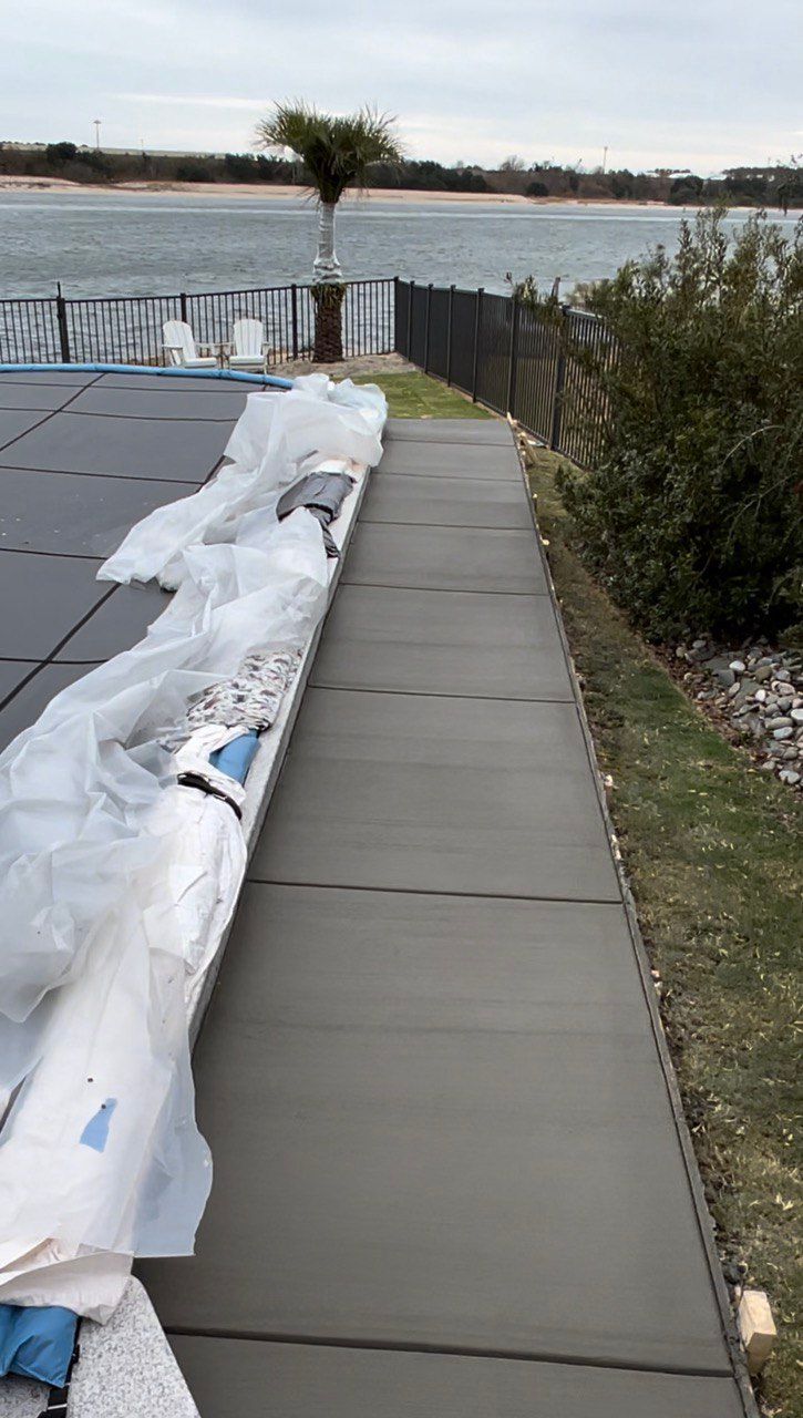 A concrete walkway leading to a swimming pool with a view of the water.