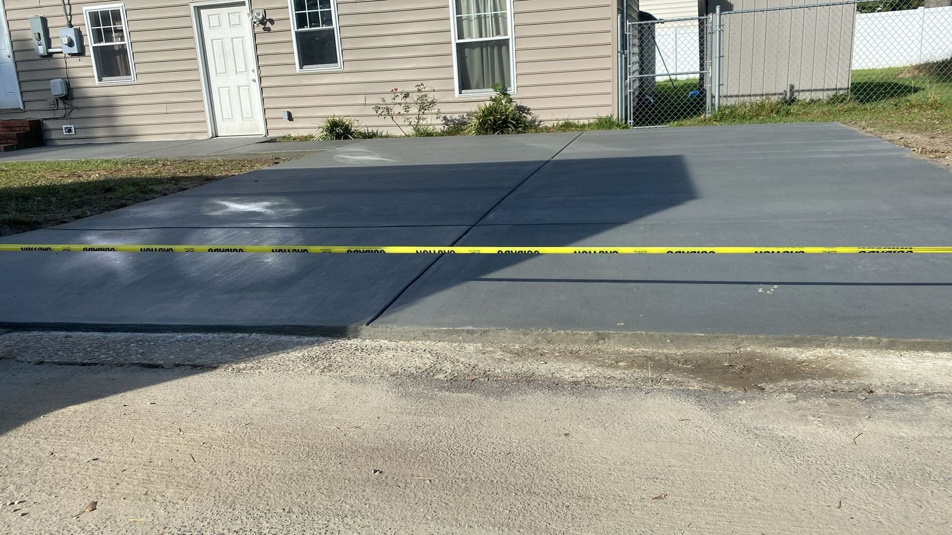 A concrete driveway in front of a house with a yellow tape.