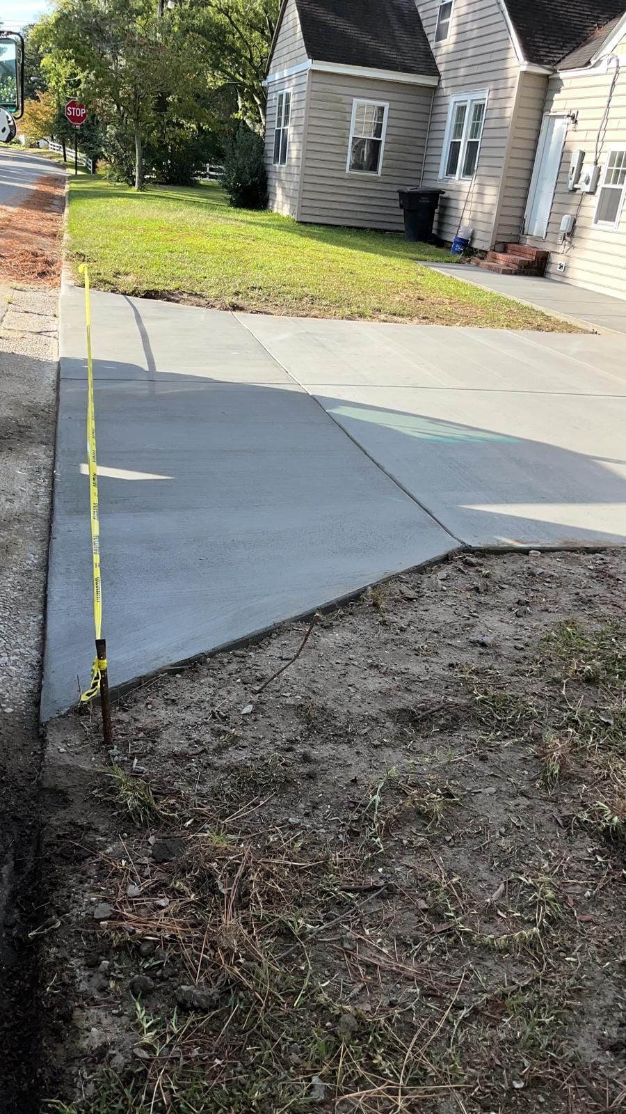 A concrete sidewalk is being measured by a tape measure in front of a house.