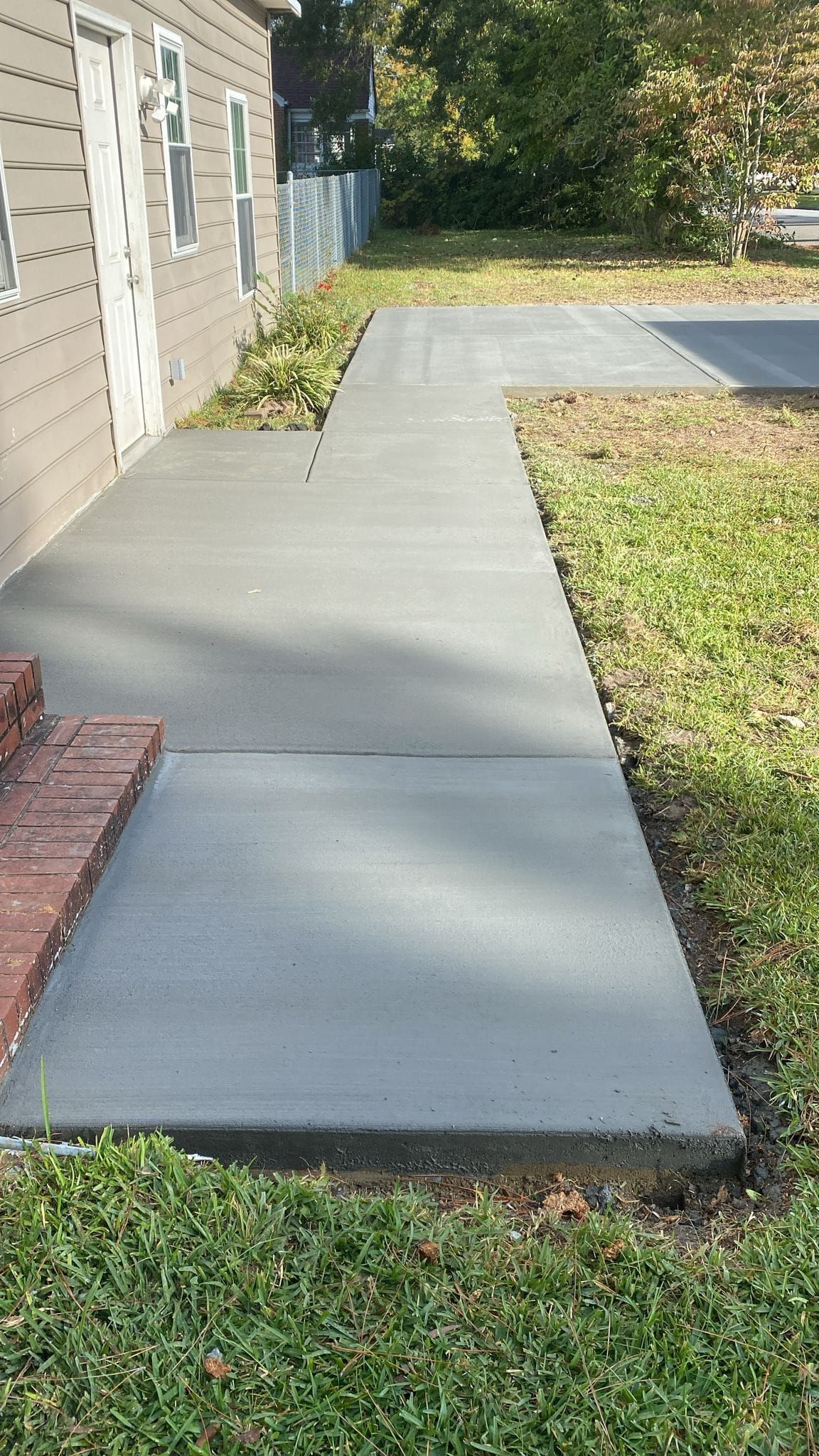 A concrete walkway leading to a house next to a grassy yard.