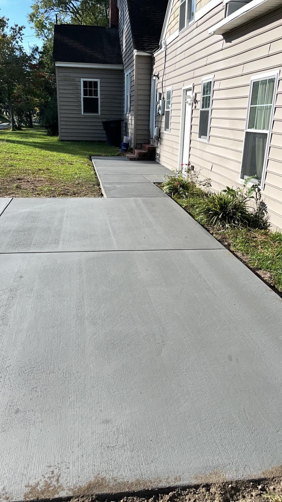 A concrete walkway leading to a house with a house in the background.