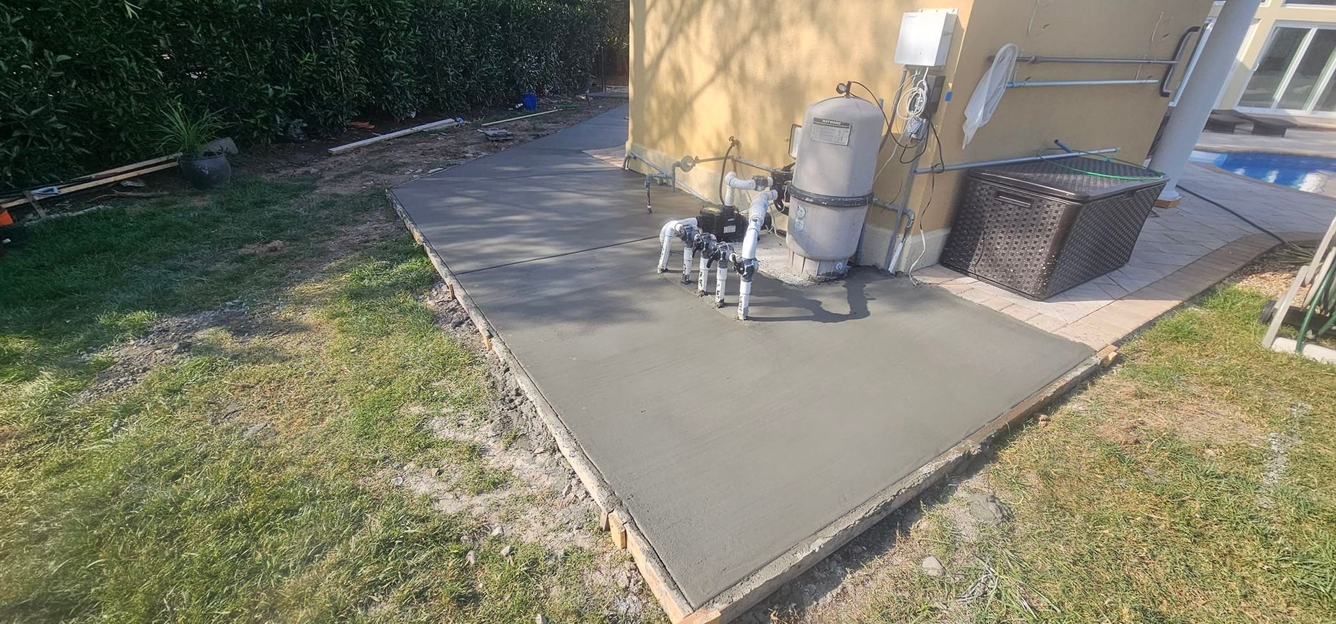 A concrete walkway is being built in a backyard next to a pool.