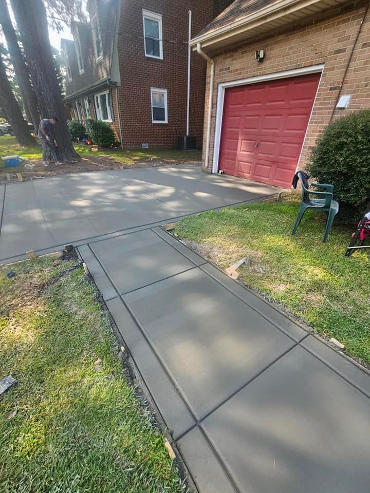 A concrete walkway leading to a red garage door next to a brick house.