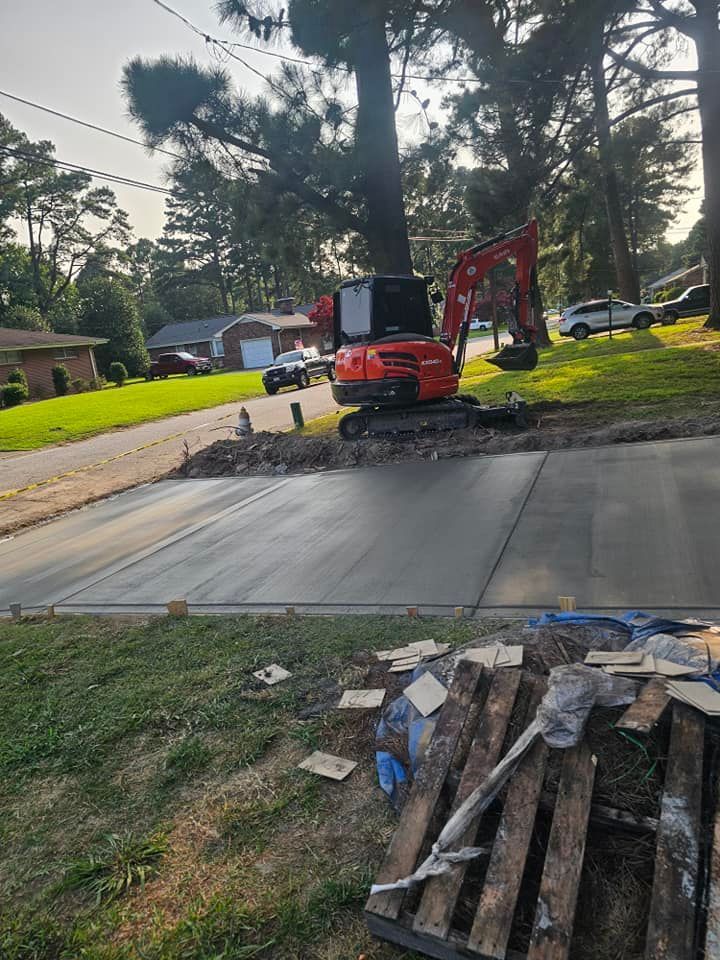 A red excavator is sitting on top of a concrete driveway.