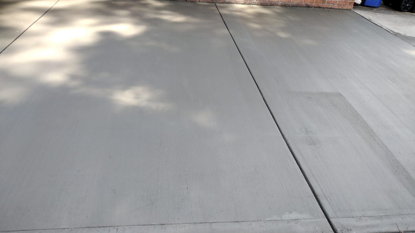 A gray concrete driveway with a tree shadow on it.