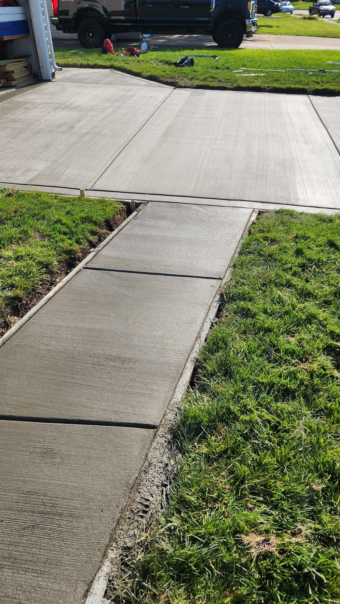 A sidewalk leading to a driveway with a car parked in the background.