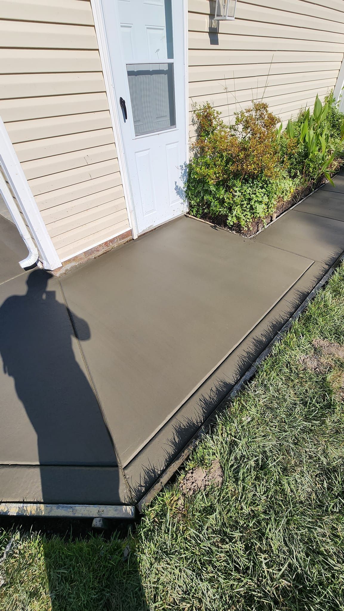 A shadow of a person is cast on a concrete sidewalk in front of a house.
