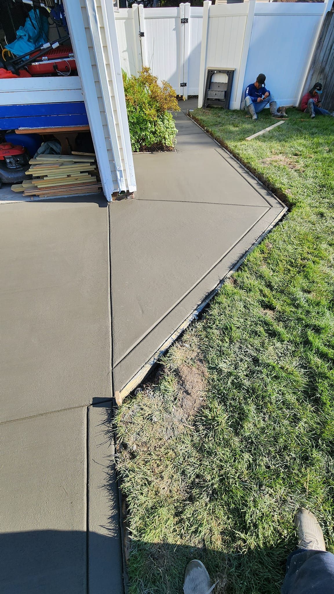 A person is standing on a sidewalk next to a fence.