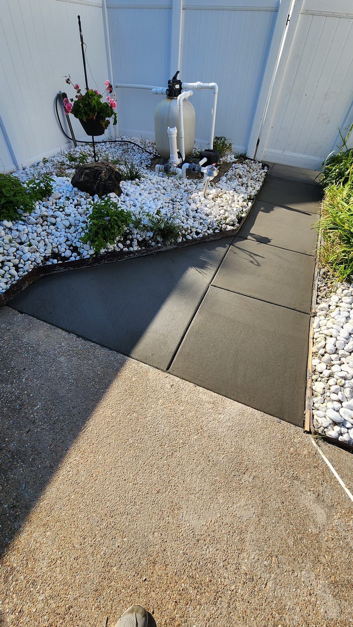 A concrete walkway leading to a garden with white rocks and plants.
