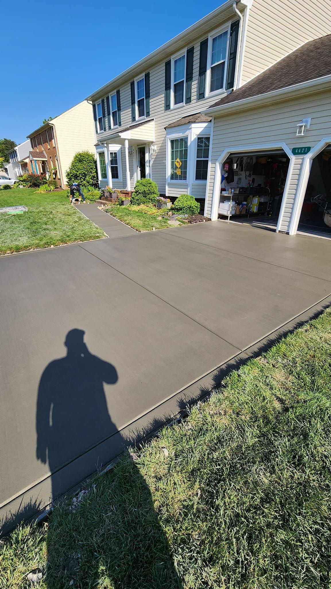 A shadow of a man is cast on a driveway in front of a house.