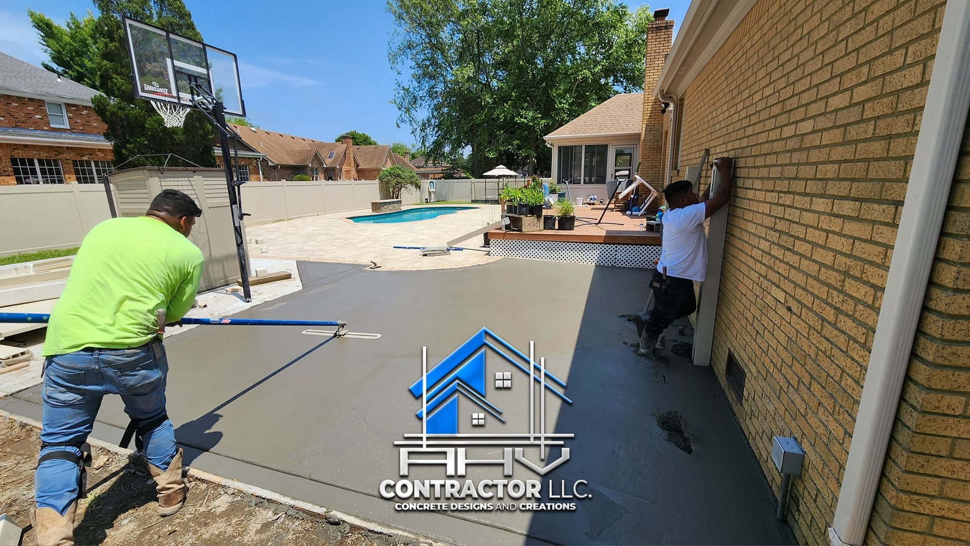 Two men are working on a concrete driveway in front of a brick house.