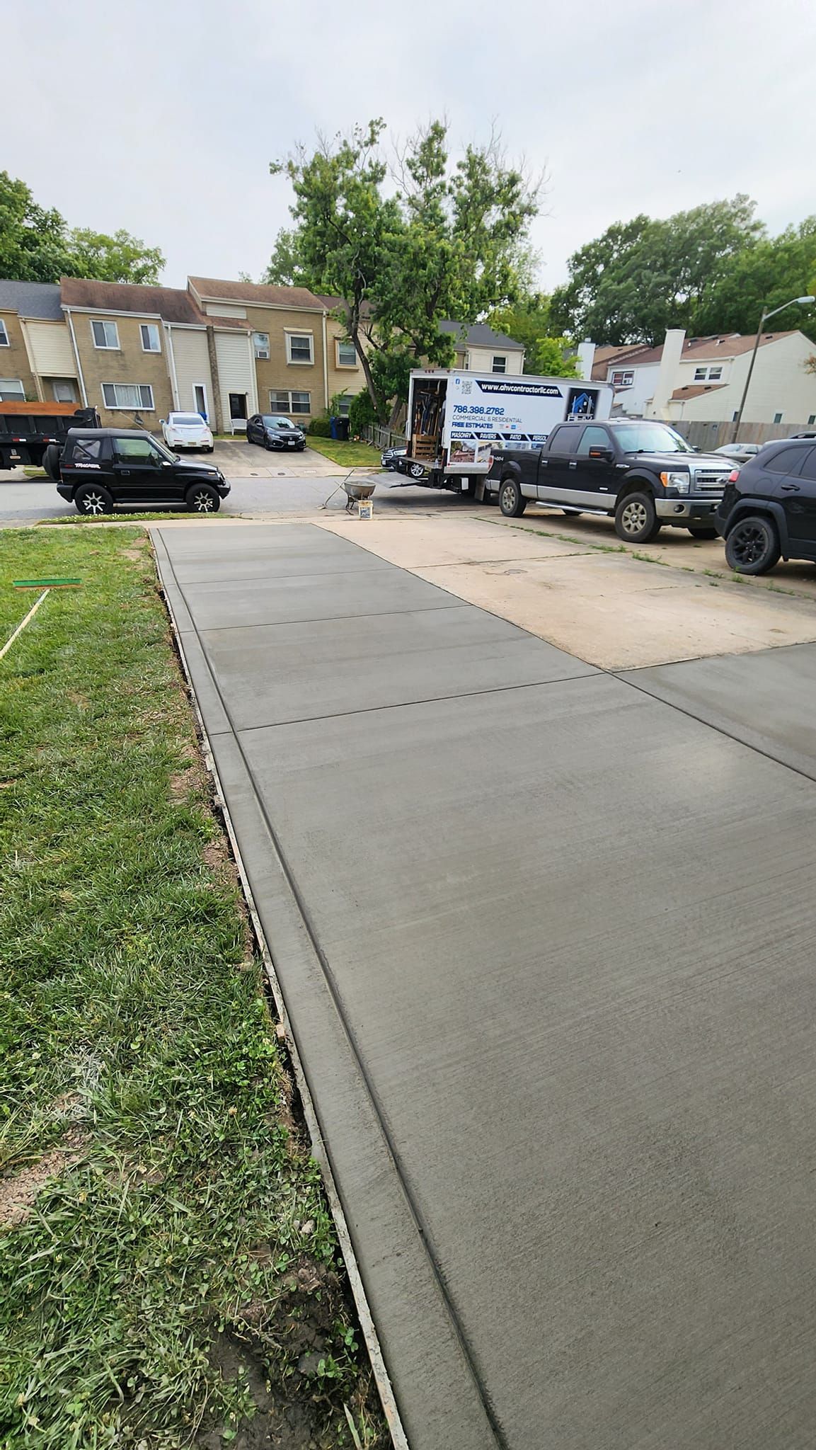 A row of cars are parked on the side of the road next to a sidewalk.