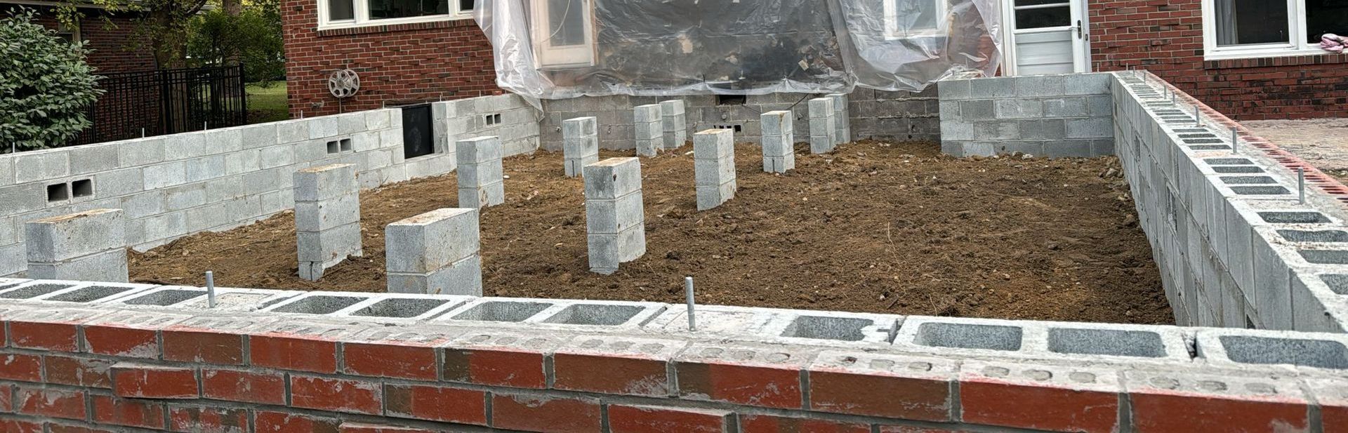 Foundation construction site with cinder block walls and concrete pillars, dirt in the middle.