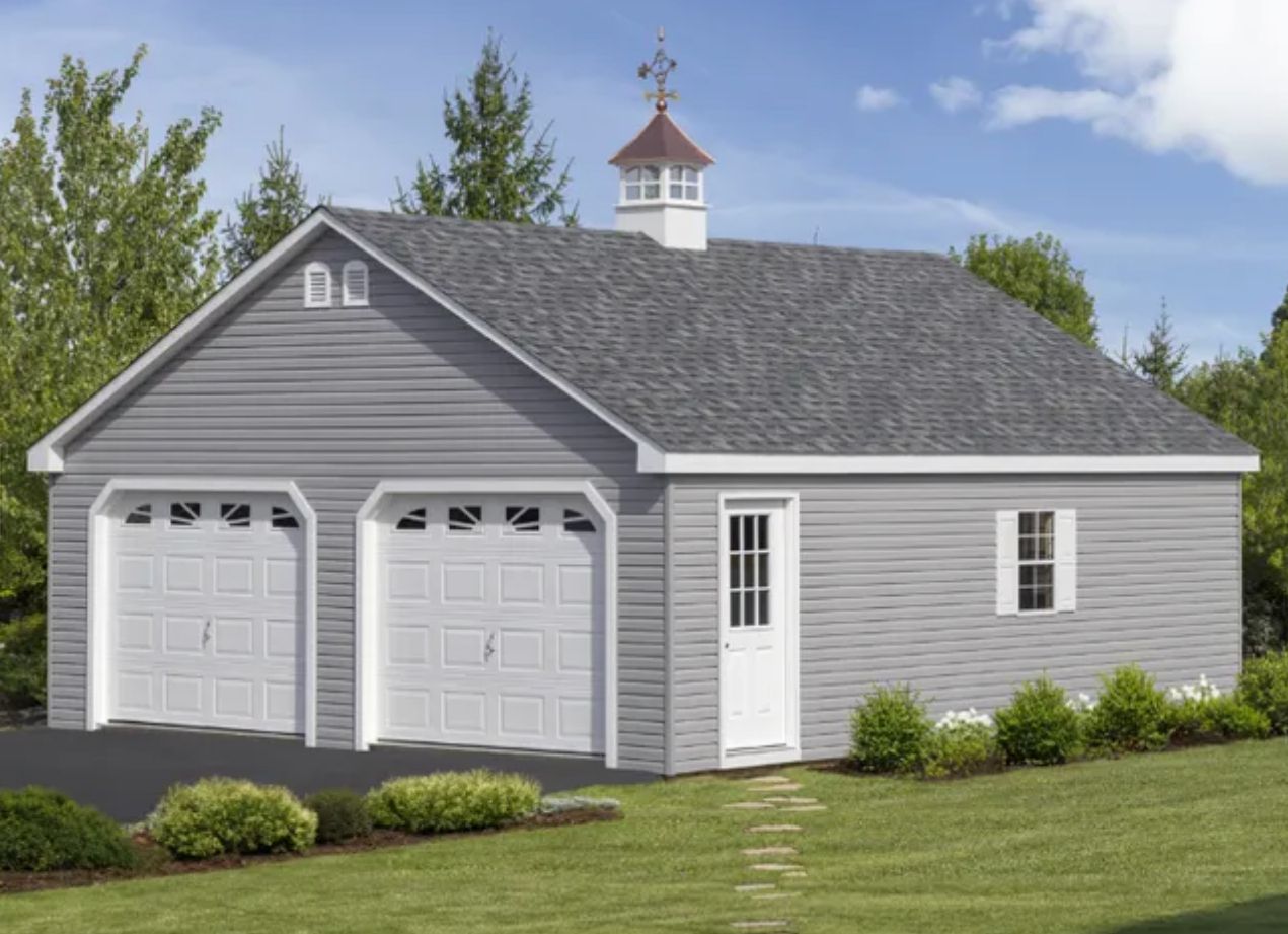 Gray detached two-car garage with white trim and a cupola in a grassy yard