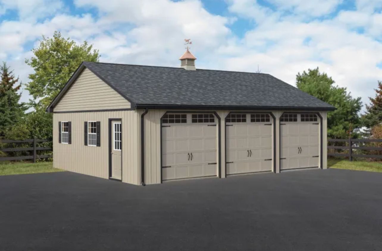 Beige detached garage with three doors and dark shingled roof on a paved driveway