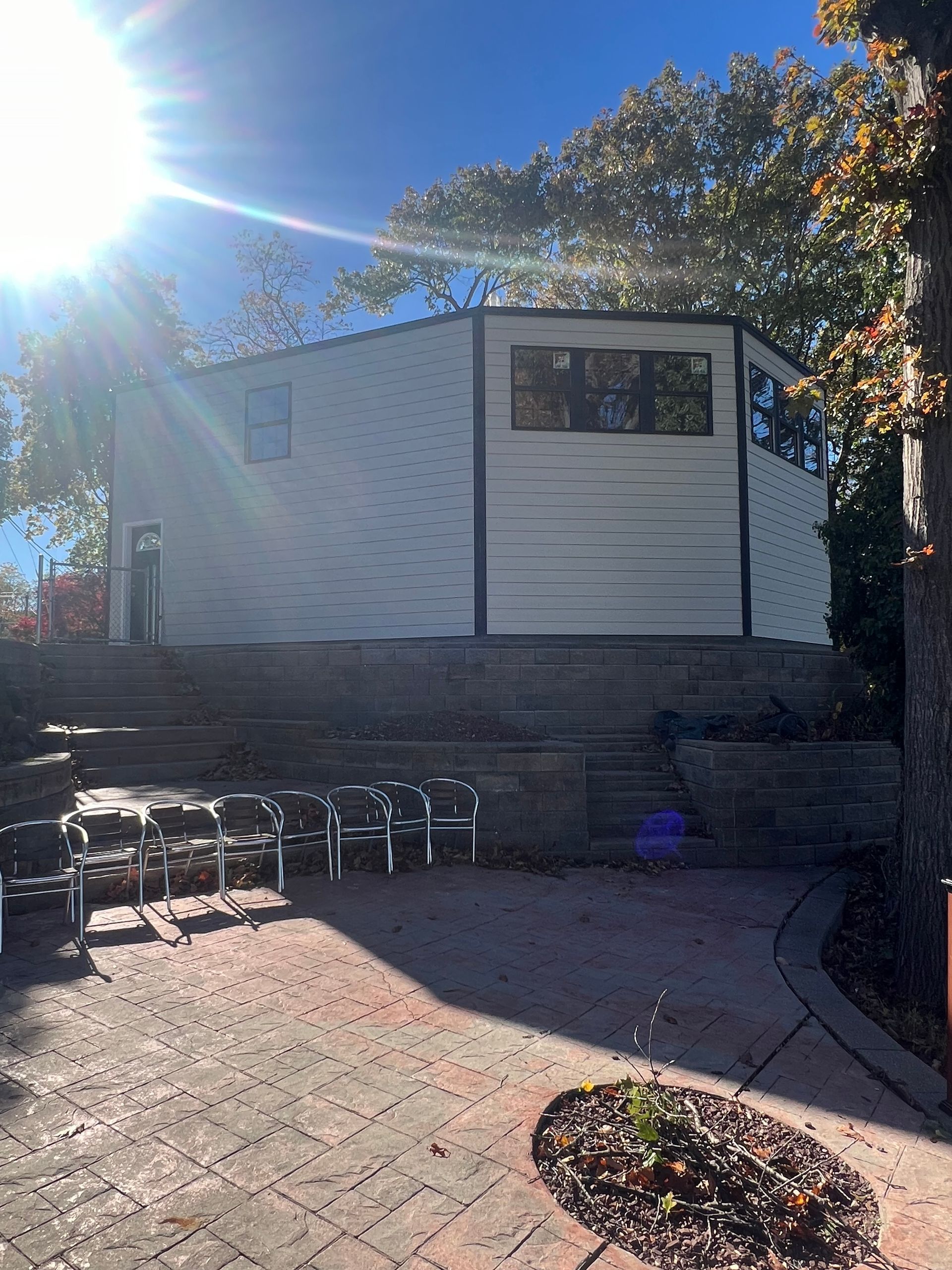 Sunlit brick patio with benches, a white building, and trees casting shadows.