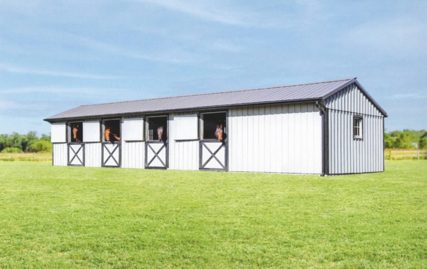 White barn with four stalls in a green field under a blue sky