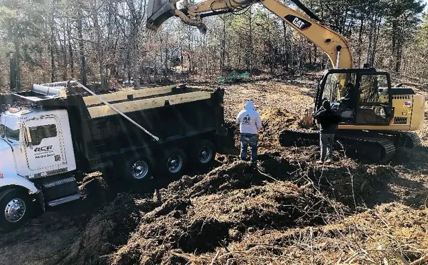 Excavator and dump truck at a muddy construction site with a worker standing nearby