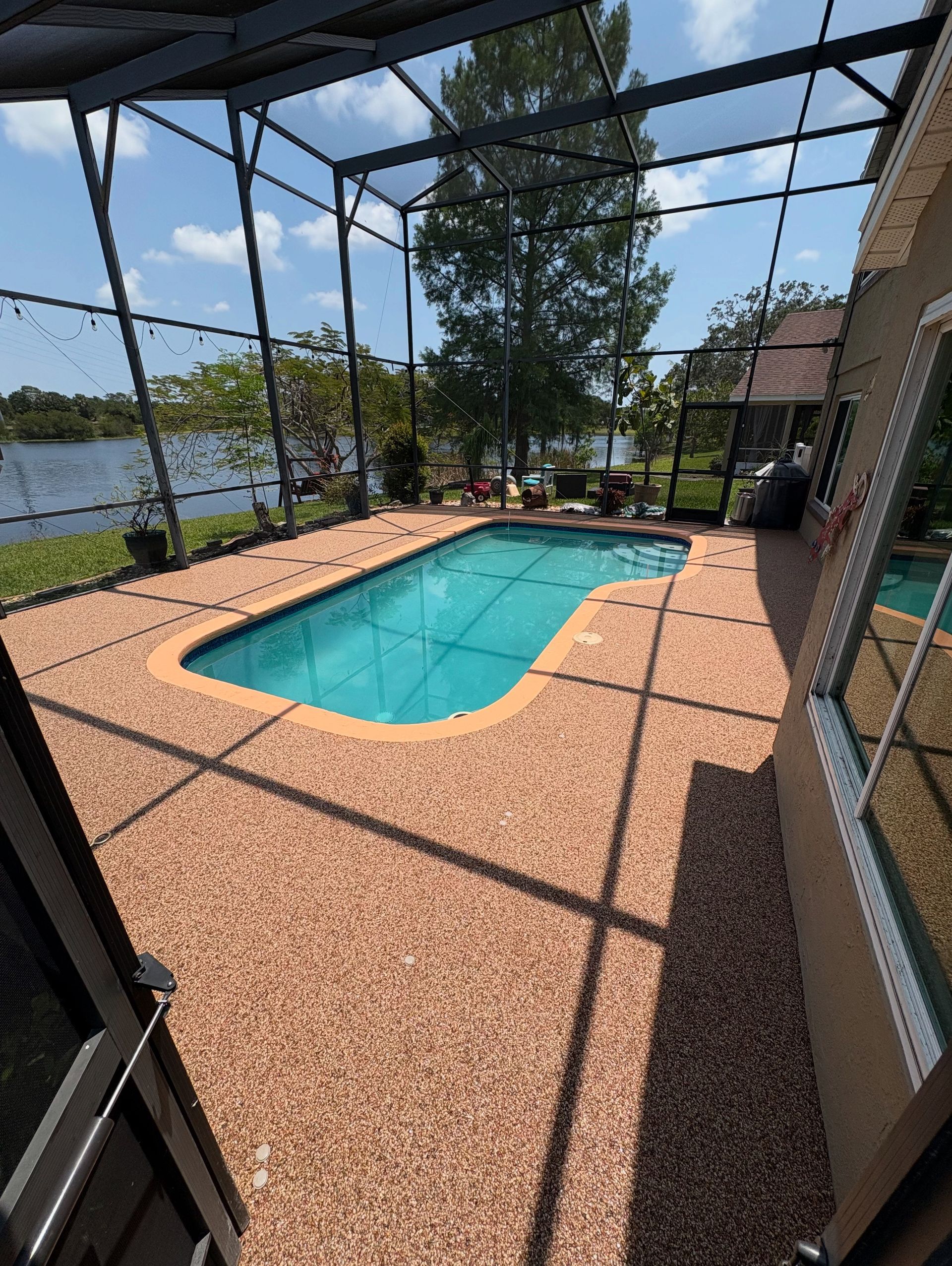 Screened-in backyard pool with blue water, tan pavers, and lake view beyond the patio.