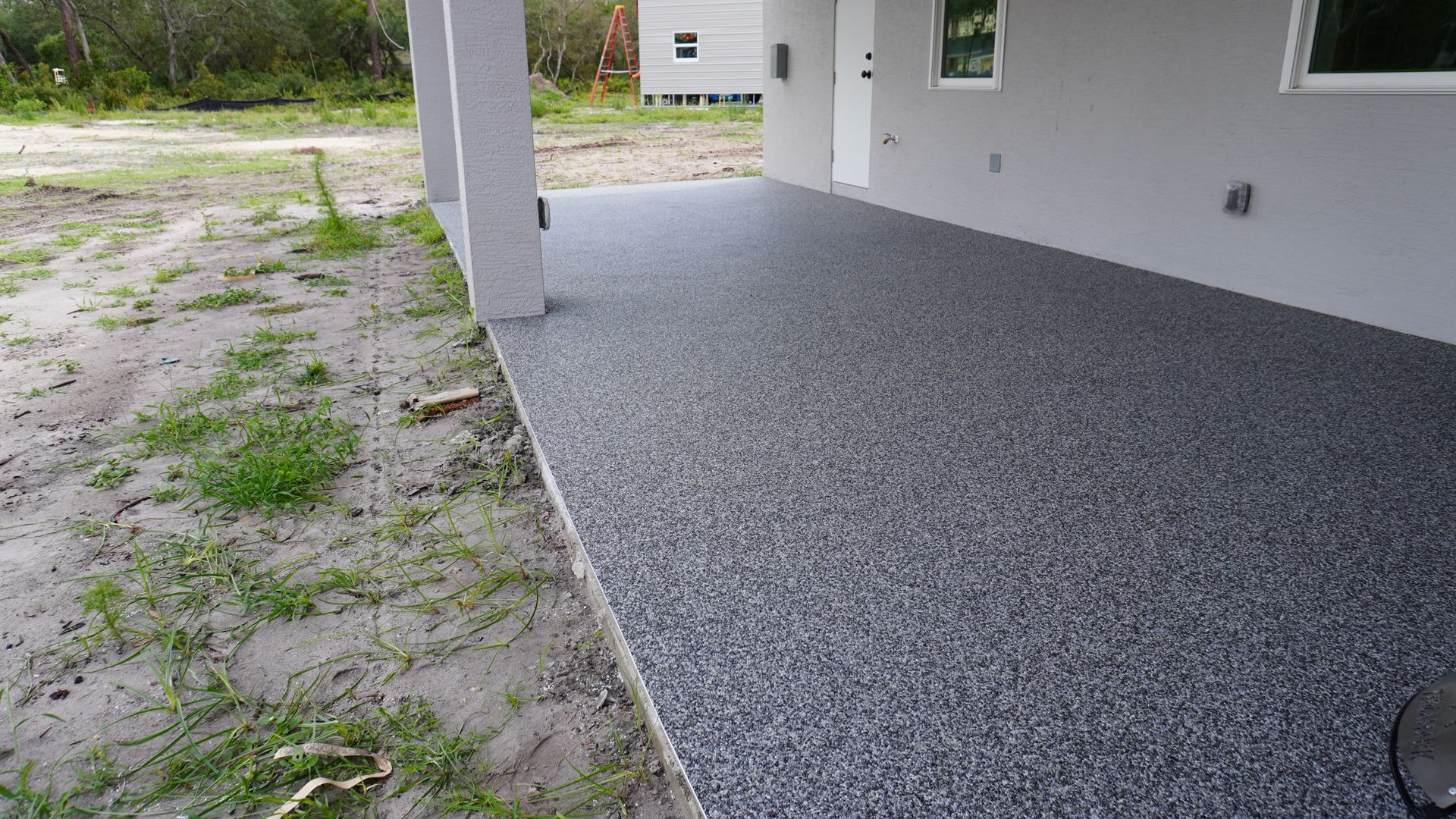 Covered concrete patio beside a gravel yard and white house wall