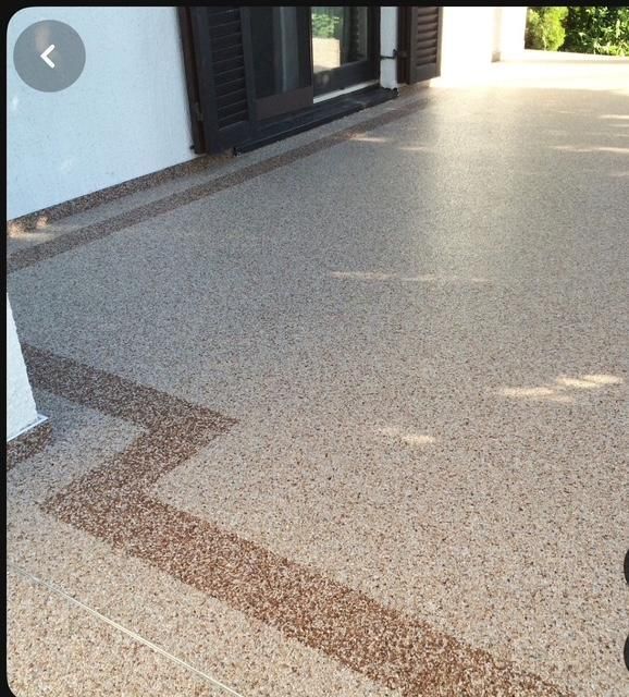 Terrazzo porch floor with a zigzag brown border beside white walls and dark shutters in sunlight