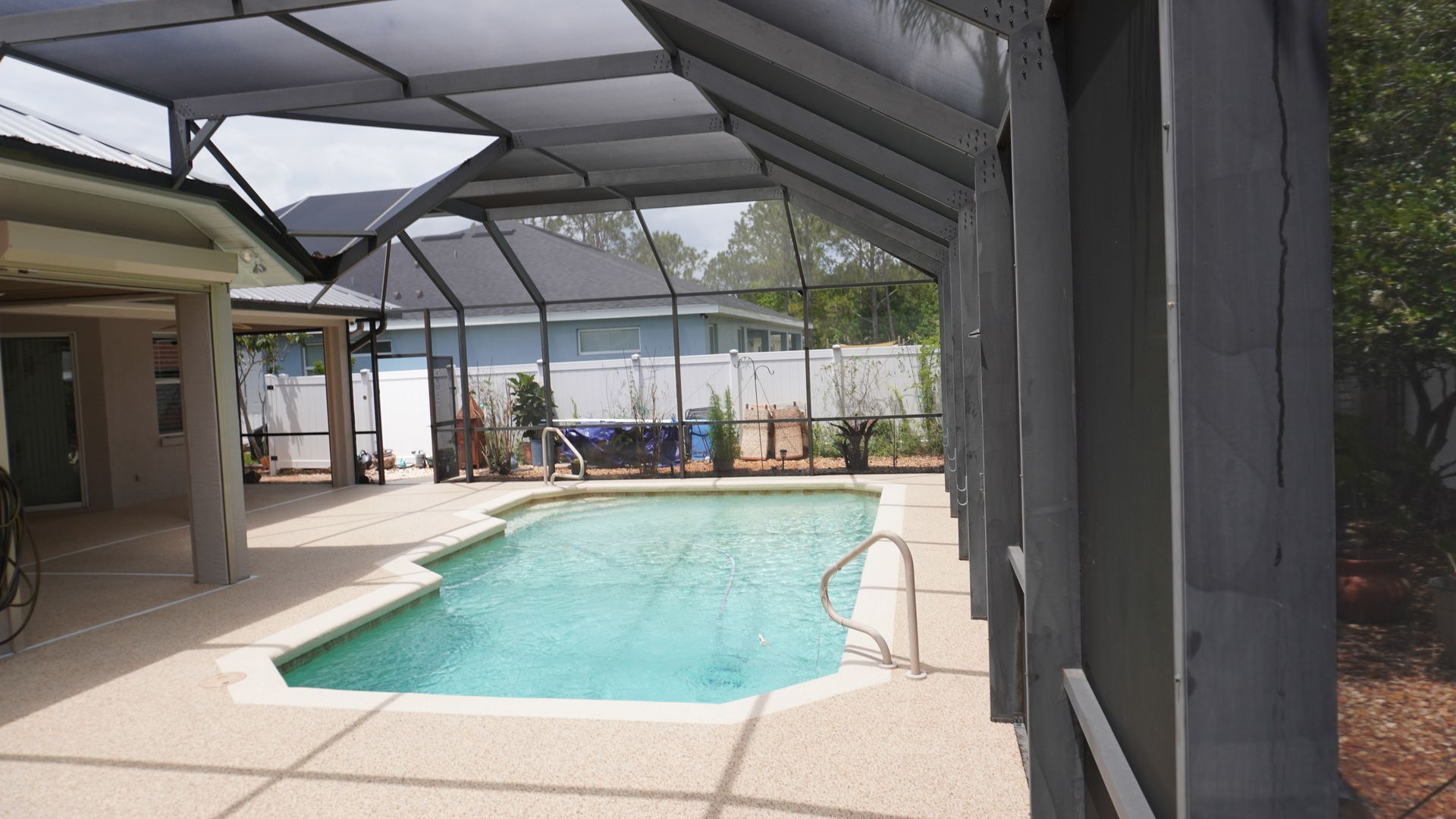 Covered outdoor pool with turquoise water, screened lanai, and patio area beside a house.