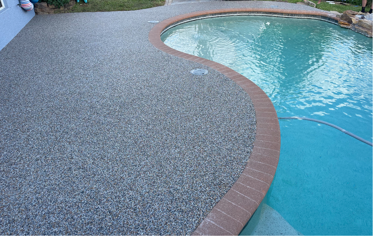 Curved pool edge with red brick border beside a gravel patio and blue water
