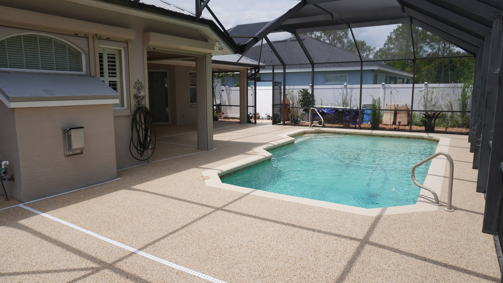 Backyard swimming pool beside a house, with a covered patio and lounge chairs under a screen enclosure.