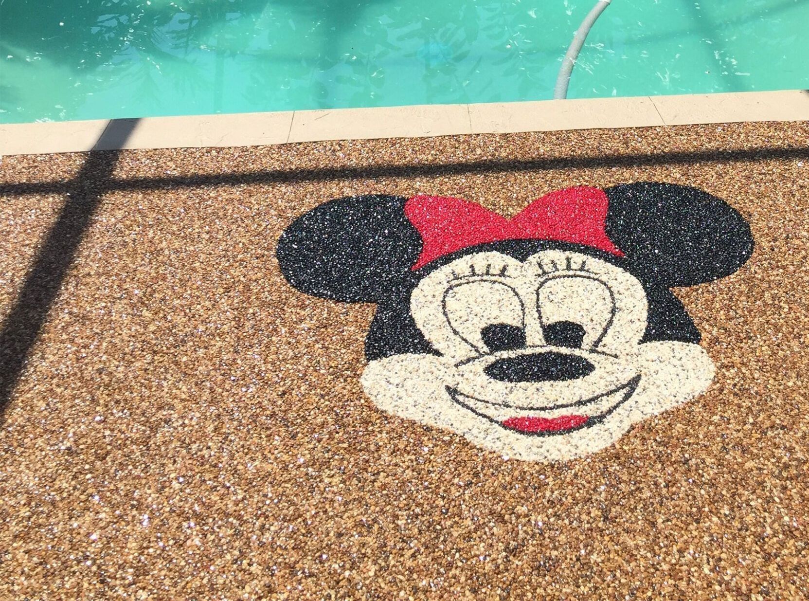 Mickey Mouse face mosaic beside a turquoise swimming pool