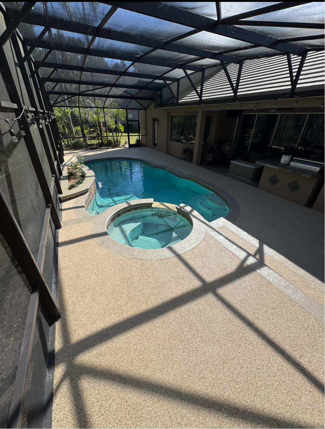 Covered patio with a small blue pool and circular hot tub, sunlit under a screened roof.