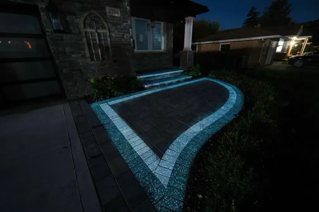Nighttime view of a glowing blue mosaic pool or fountain beside a house patio