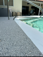 Textured gray pool deck beside clear blue swimming pool and building entrance