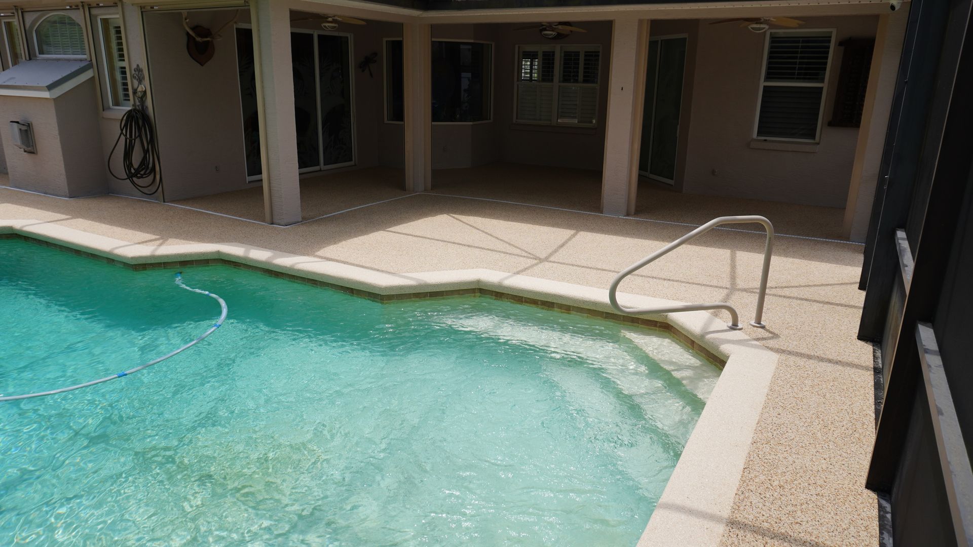 Outdoor pool with turquoise water beside a beige patio and metal handrail under a covered walkway