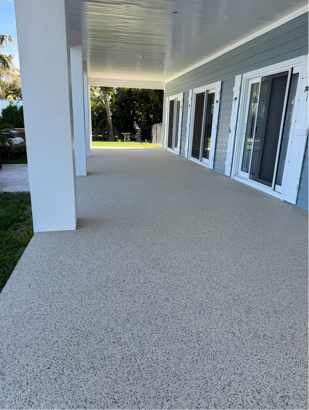 Covered porch with white columns, gray speckled flooring, and glass double doors along the side of a building