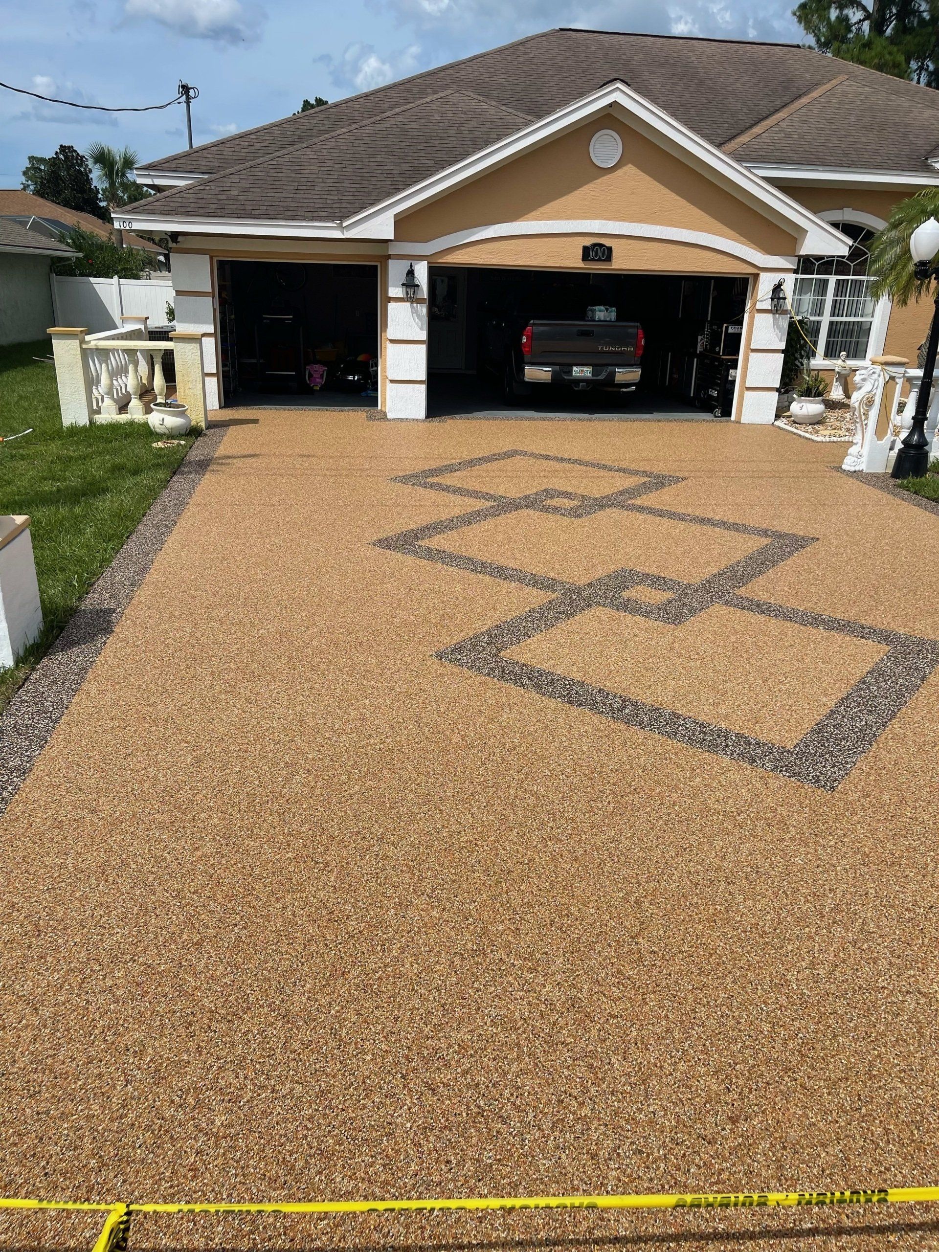 House with open garage and newly coated tan driveway, outlined with masking tape, viewed from the street.