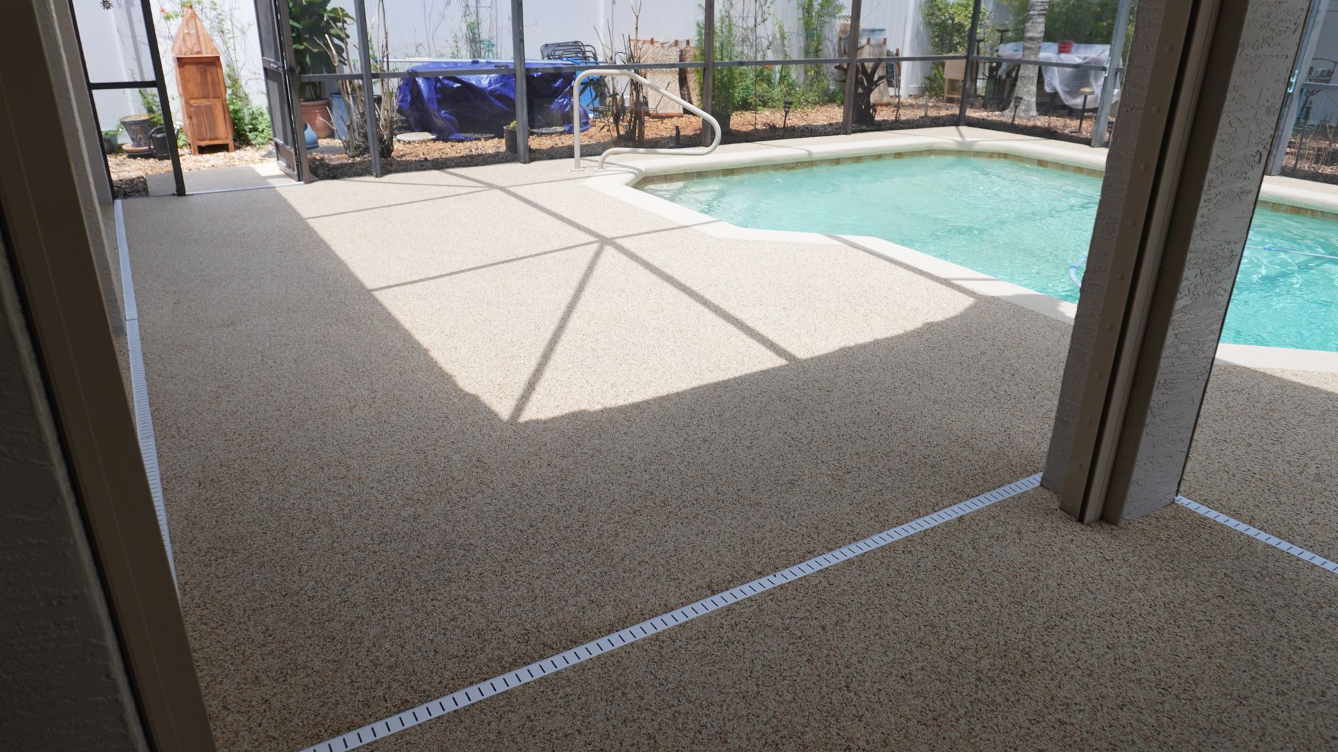 Covered patio overlooking a backyard pool with sunlit concrete and lounge chairs