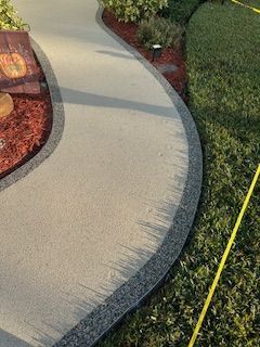 Curved concrete walkway edging a landscaped yard with red mulch, plants, and a yellow tape line