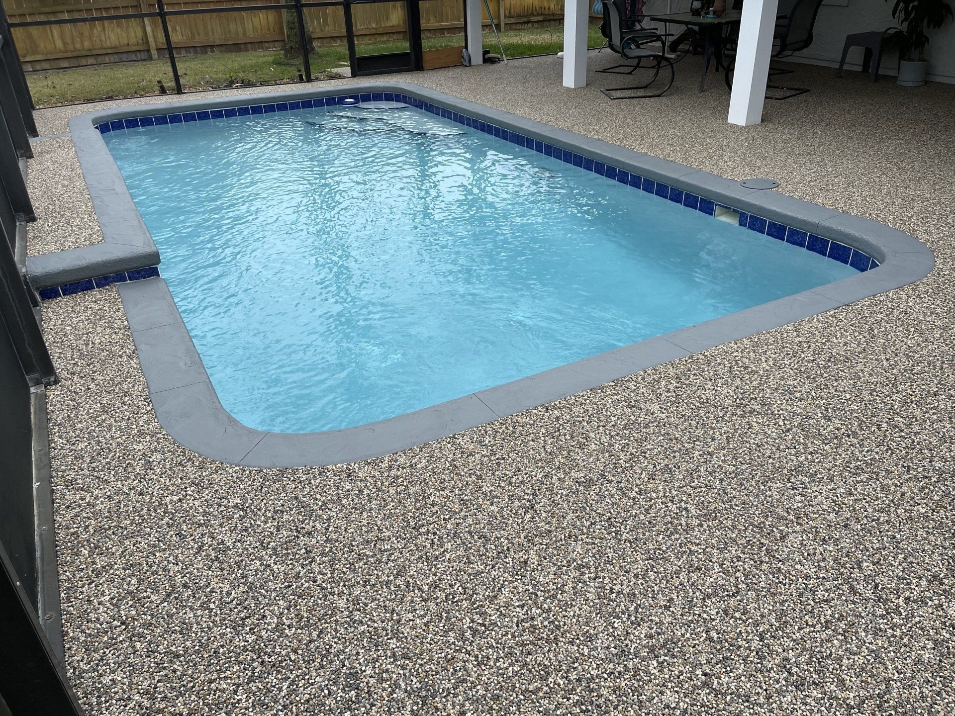 Small backyard swimming pool with light blue water and a pebble deck