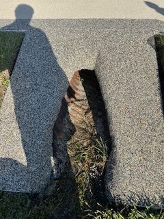 Cracked gray concrete walkway with a large hole exposing dirt and grass below