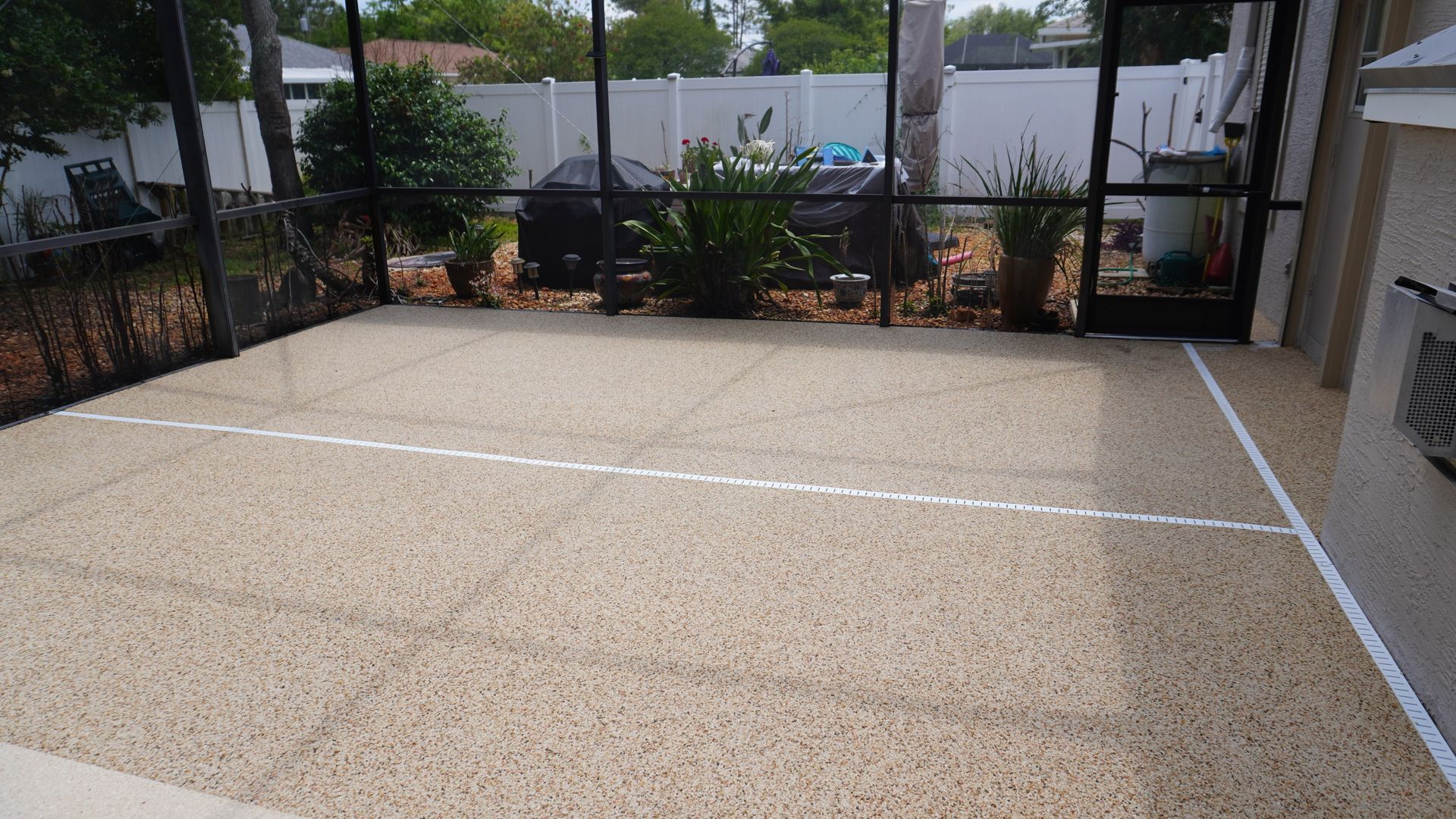 Empty tan court with white boundary lines beside a chain-link fence and patio area