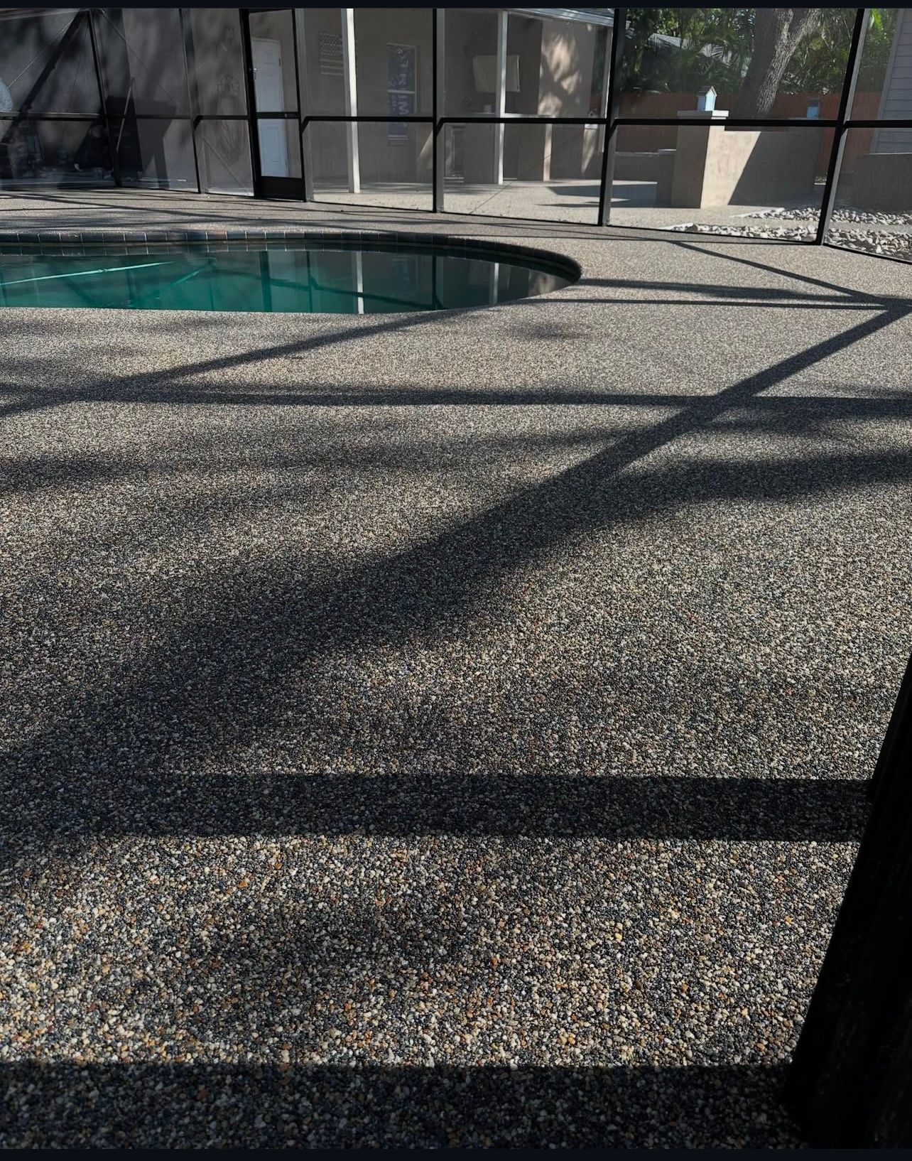 Poolside patio with textured concrete, diagonal shadows, and a screened-in pool area.