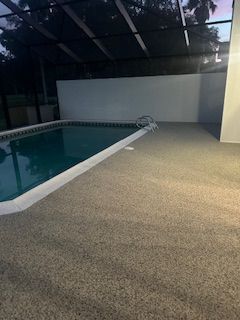Indoor pool with turquoise water beside a beige deck and dark glass enclosure