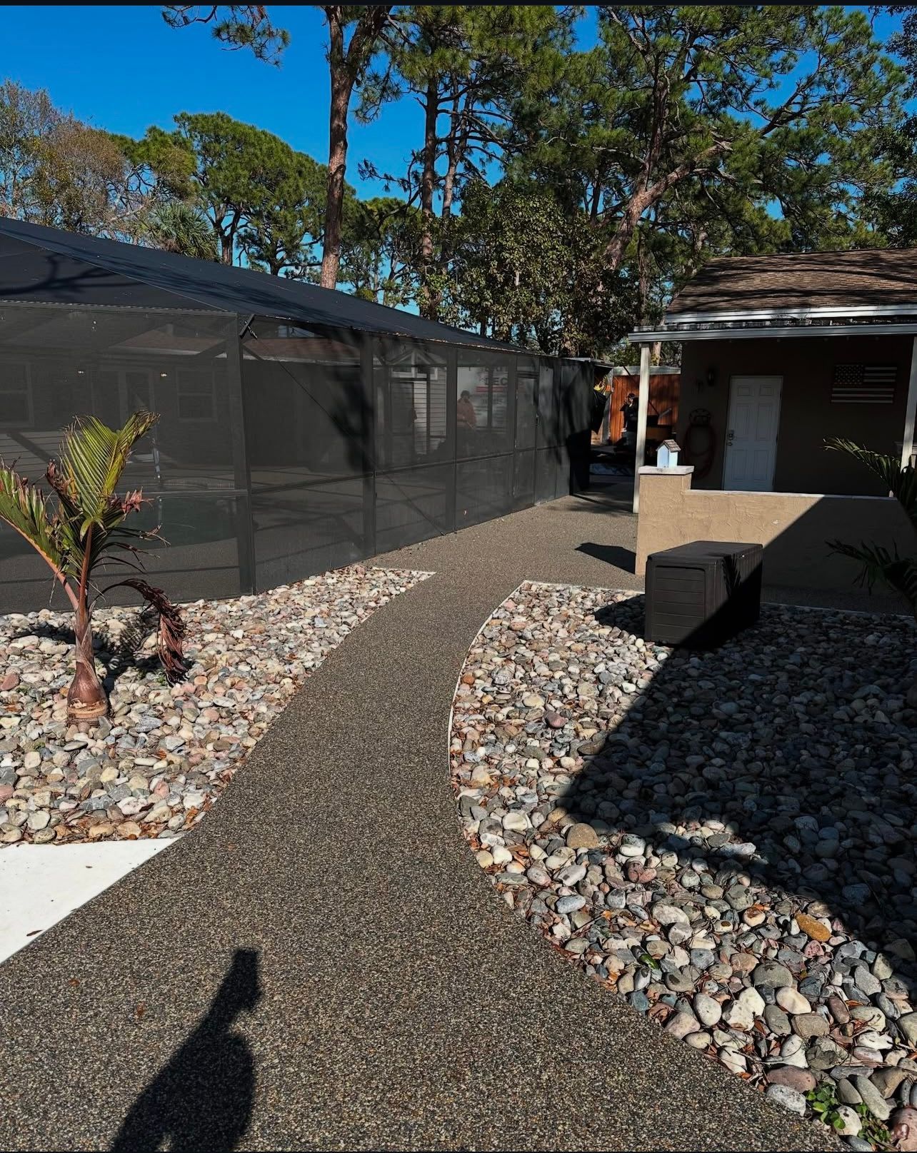 Curved gravel path between screened buildings and a house in a sunny yard