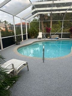 Screened backyard pool with white lounge chairs and tropical plants