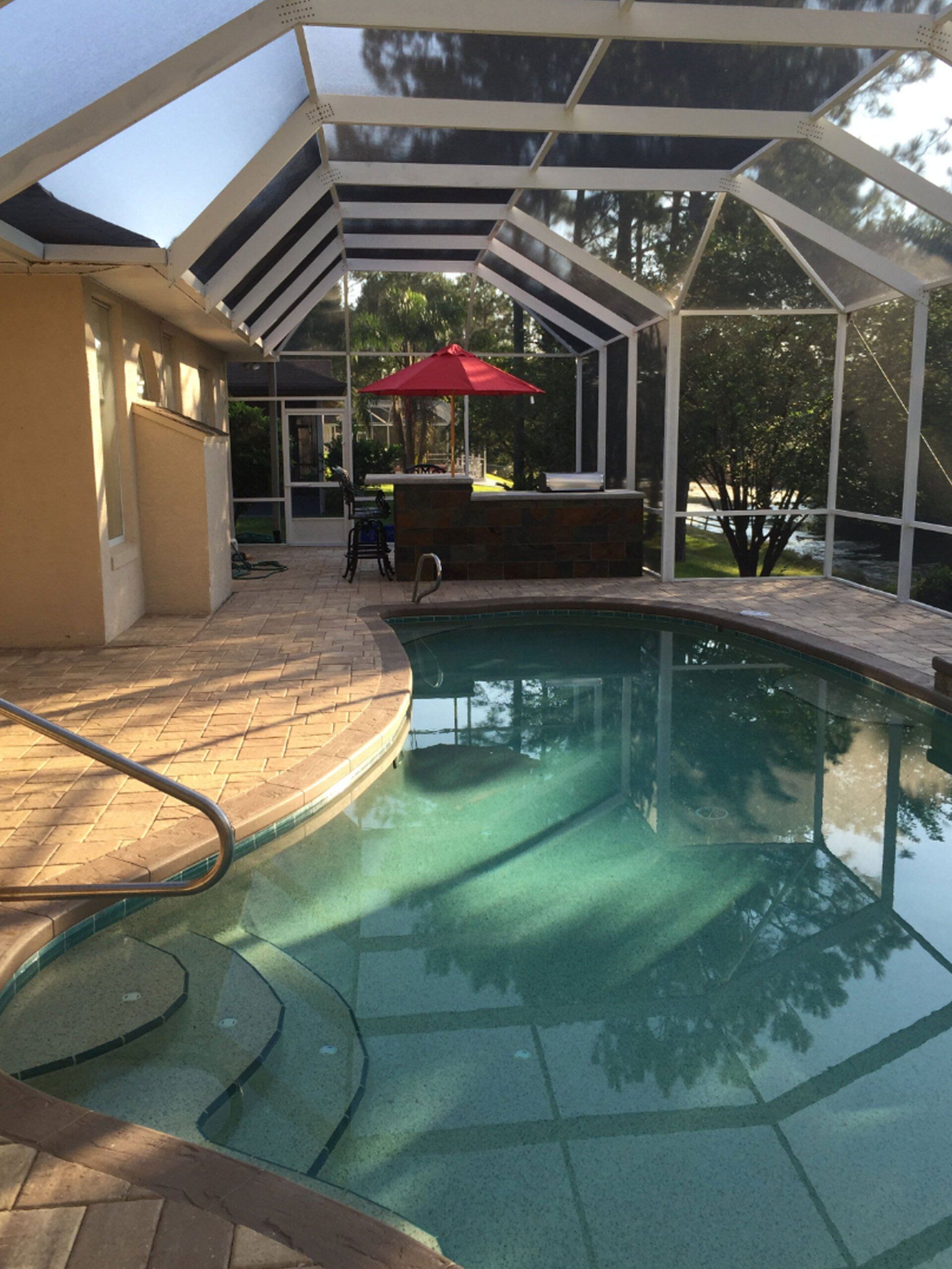 Backyard pool with white canopy, patio, and red umbrella beside a sunlit house.