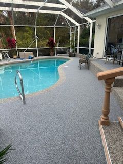 Screened-in pool with blue water, gray deck, and patio chairs beside a house